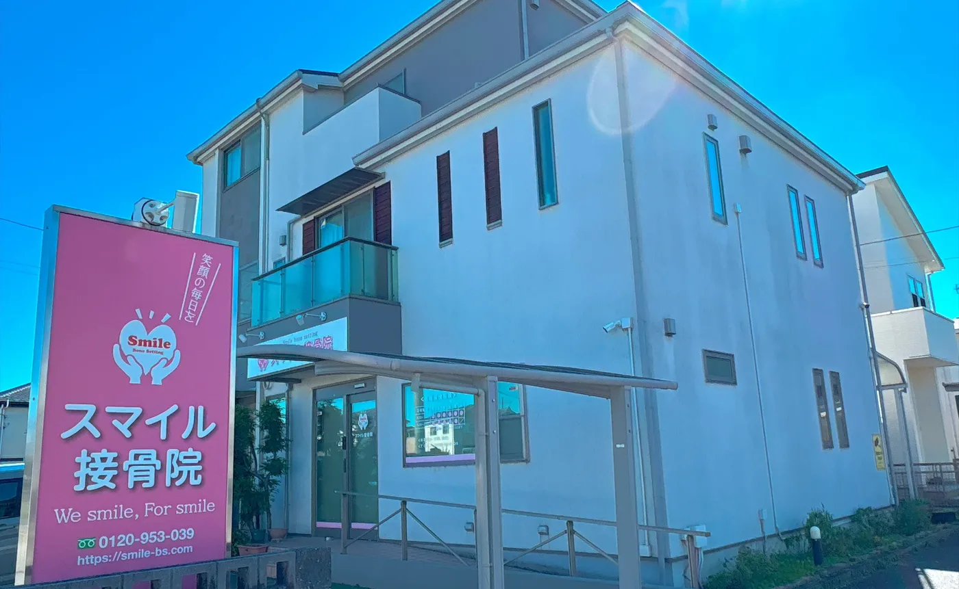 スマイル接骨院の外観。ピンクの看板とカーポートのある白い建物